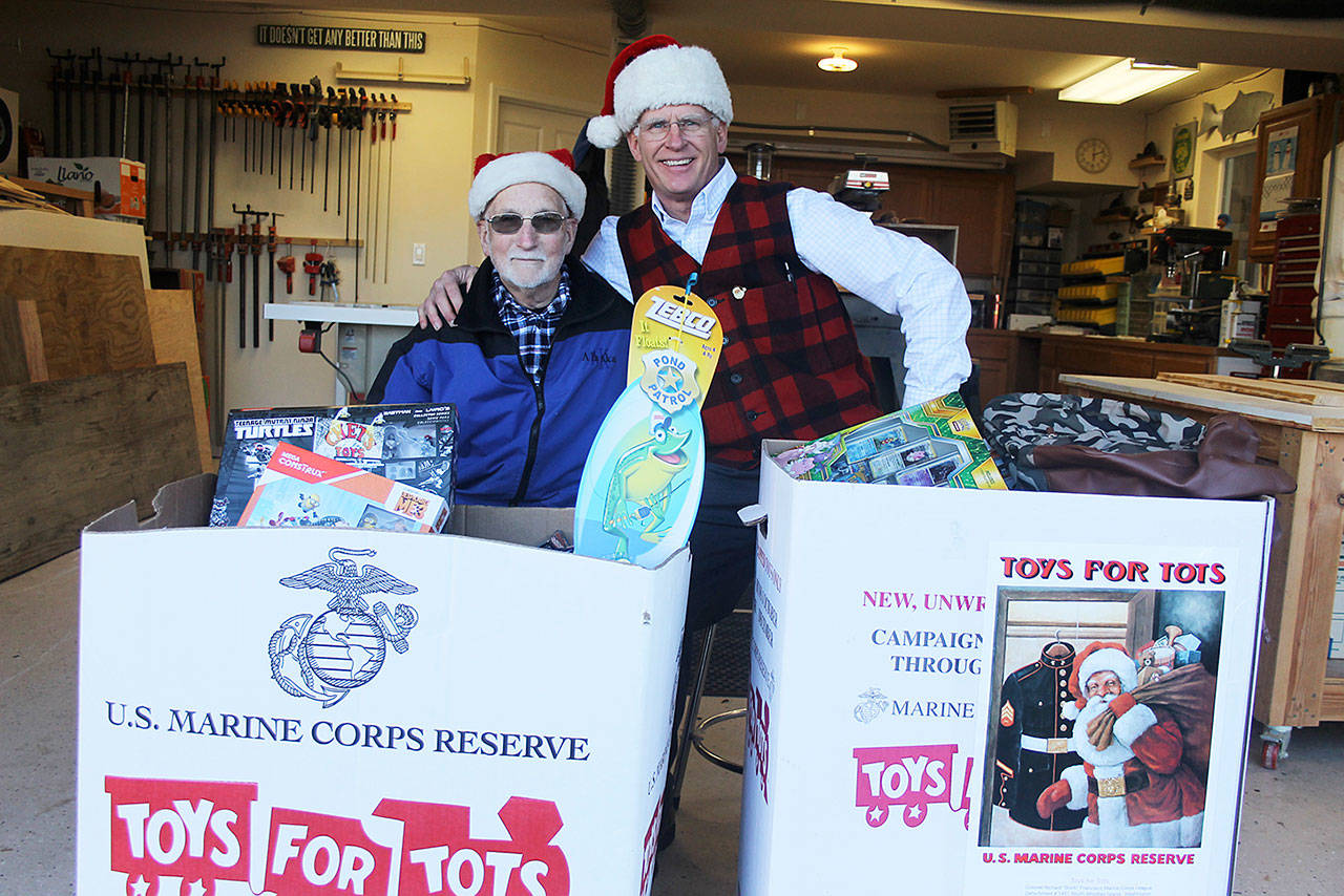Evan Thompson / The Record — Ron Whitman and Kevin Lungren of The Fishin’ Club pose for a shot behind two boxes of toys collected by Toys for Tots, a program run by Col. Richard “Buck” Francisco Marine Corps League Detachment No. 1451. The club’s members will make deliveries to needy families around South Whidbey before Christmas.