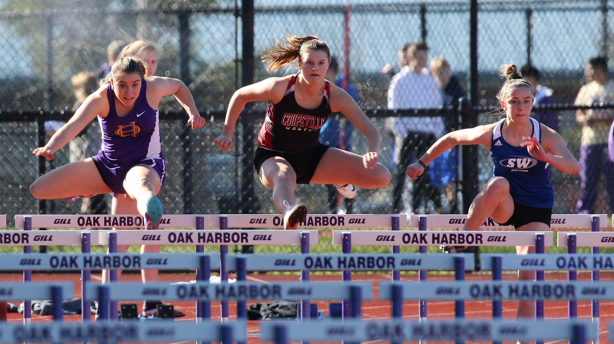 South Whidbey’s Sophia Nielsen, right, takes an early lead over Oak Harbor’s Samantha Hines, left, and Coupeville’s Lindsey Roberts on the way to winning the 100 hurdles. (Photo by John Fisken)