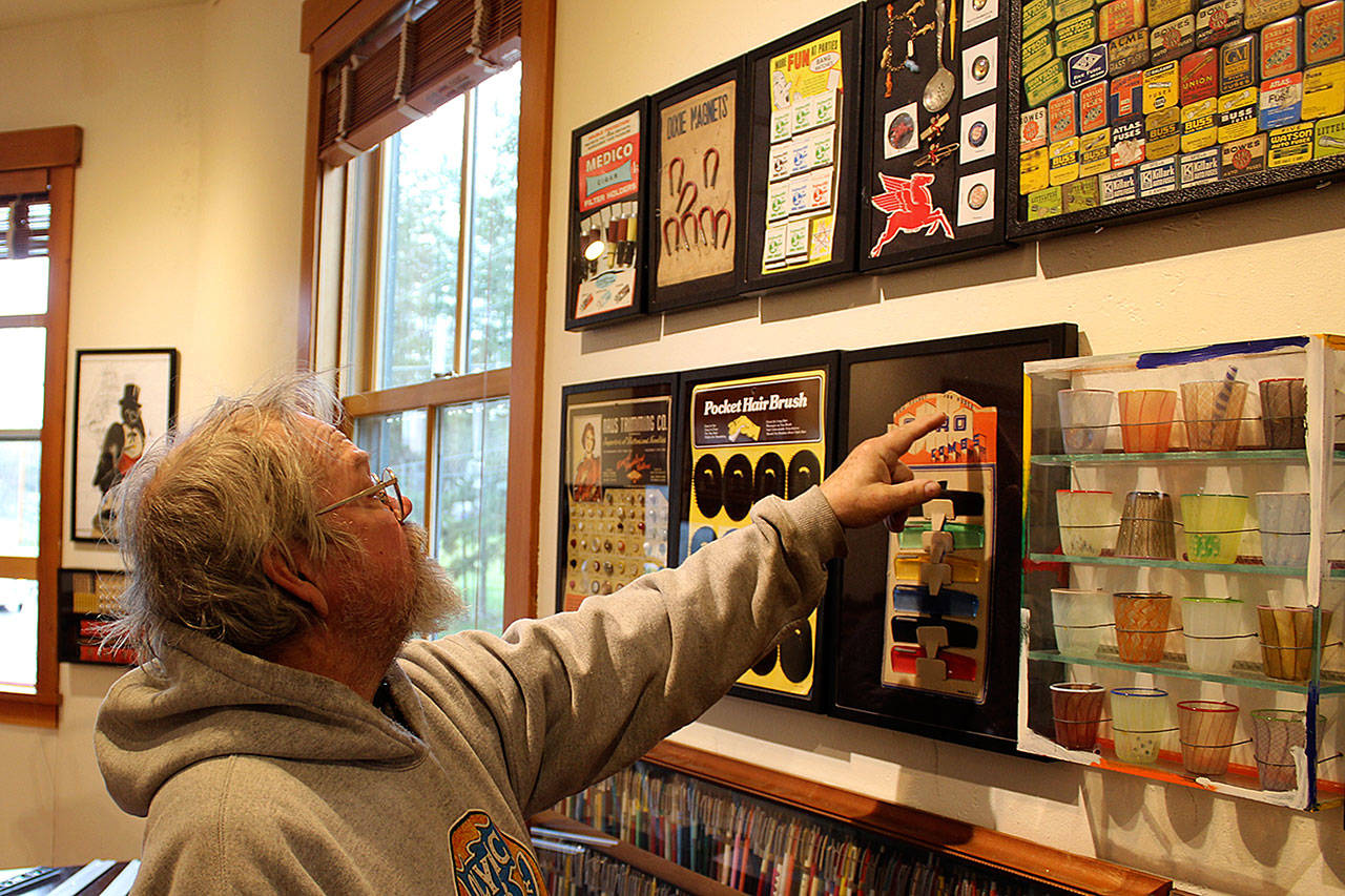 Richard Marquis looks over the arrangement of his “Found Objects” installation at Bayview Corner’s Front Room Gallery. A Freeland glass artist with pieces in galleries worldwide, he’s also collected quirky advertising and other items. Photo by Patricia Guthrie/Whidbey News Group