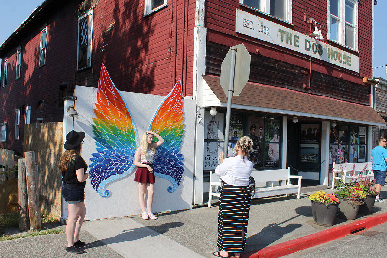 Canadian tourists stop to pose with colorful wings that mysteriously appeared overnight in Langley near The Dog House that’s undergoing renovation. Elaine Moore takes a photo of her daughter, Kelaynna Kikkert, as her friend, Marisa Quagla, left, looks on. (Photo by Patricia Guthrie/Whidbey News Group)