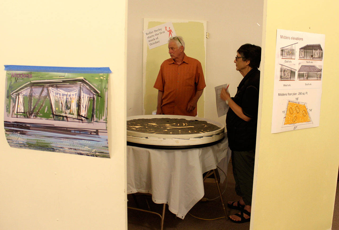 Jay Devenny talks about his creation called “Sand Dabber ” with Diane Divelbess at a Wednesday meeting discussing proposed improvements to Seawall Park. To the left is a drawing of his “Middens” shelter idea. (Photo by Patricia Guthrie/Whidbey News Group)