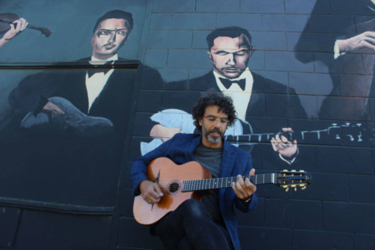 Troy Chapman plays in front of Langley’s mural devoted to Django Reinhardt and DjangoFest Northwest. His band, Hot Club of Troy, performs Wednesday night at the music festival that’s honoring founder Nick Lehr this year.The mural was painted by Matt Statz several years ago. (Photo by Patricia Guthrie/Whidbey News Group)