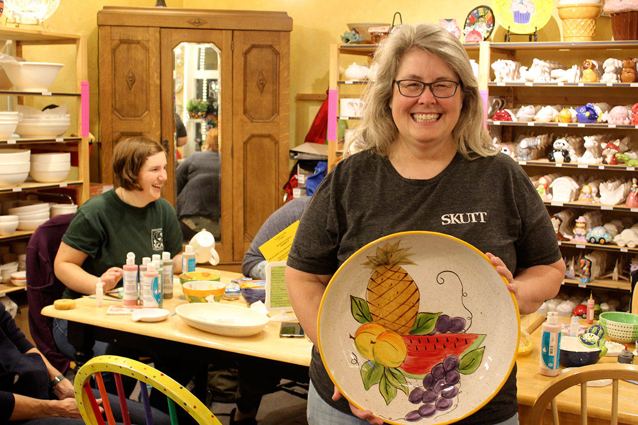 Tina Beard, who is selling her longtime business, Art Escape, shows off one of the many pieces she painted over the years. (Photo by Patricia Guthrie/Whidbey News Group)