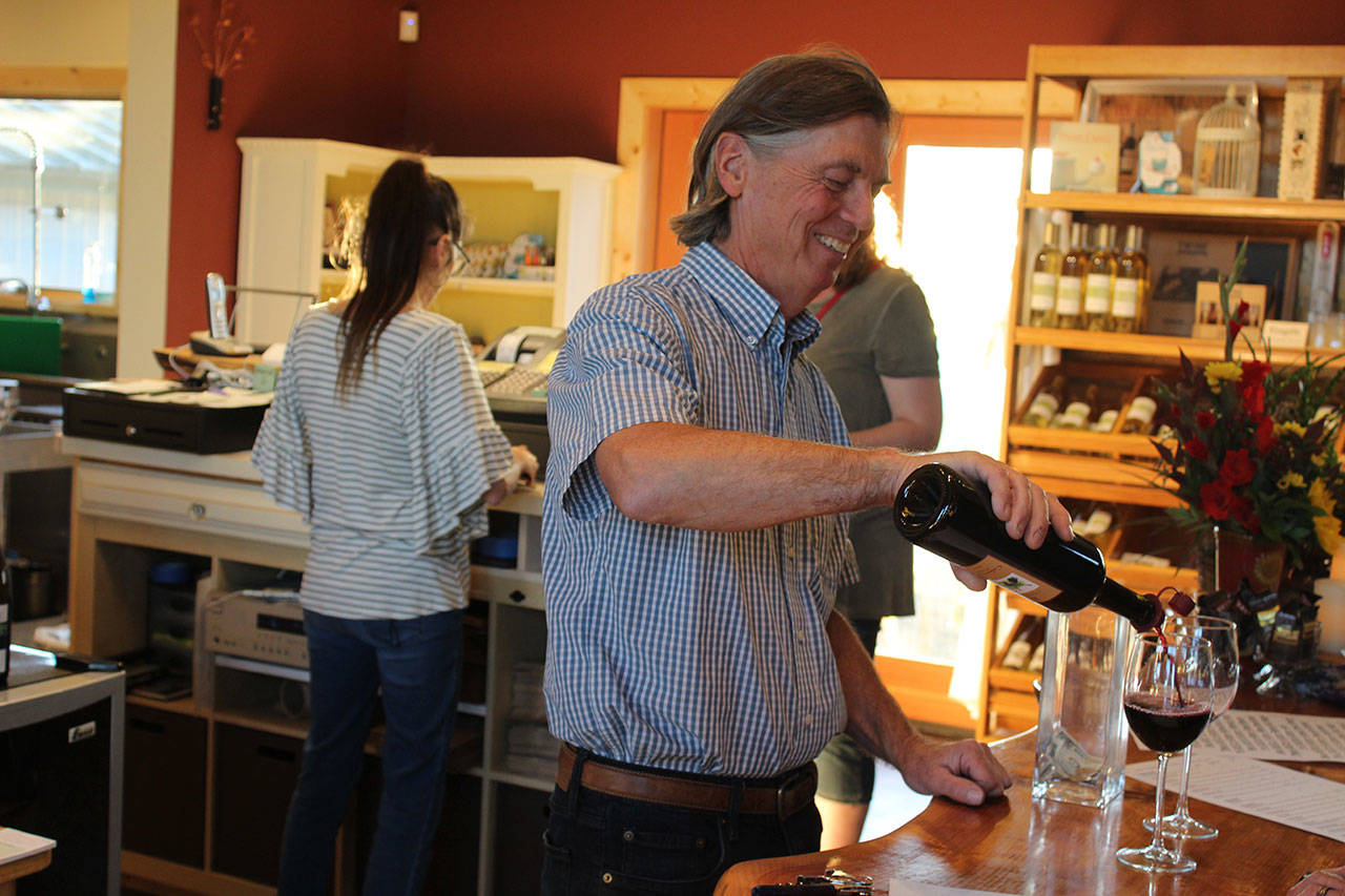 Even after 15 years of making wine, pouring wine, talking about wine and hauling cases of wine, Ken Bloom still serves a glass of wine with a smile. (Photos by Patricia Guthrie/Whidbey News Group)