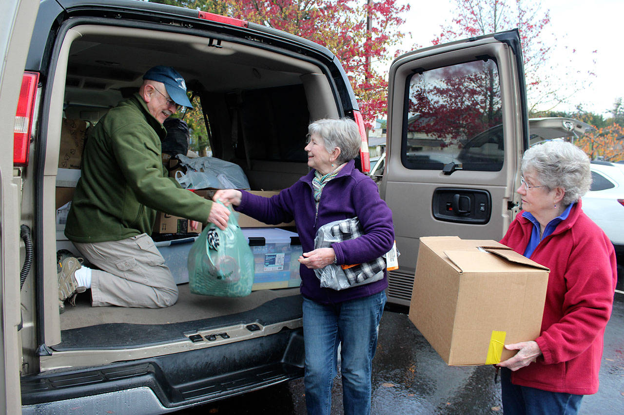 Tony Aguilar arranges donations handed to him by Jean Beers, center, and Norma Hansson. This is the third year that parishioners from three South Whidbey churches donated new clothes, personal care items and other needs for residents of Western State Hospital. (Photo by Patricia Guthrie/Whidbey News Group)