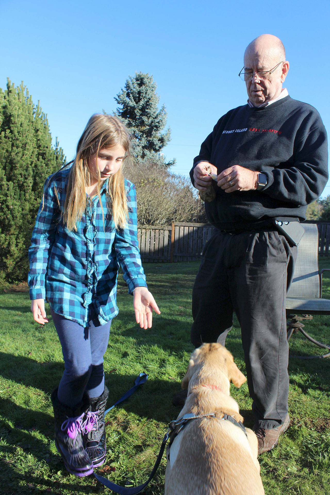 With her grandfather, Kirk Lacewell, Piper Pontius plays with Scout who she says is bound for canine stardom since making a mammoth discovery in the backyard. (Photo by Patricia Guthrie/Whidbey News Group)