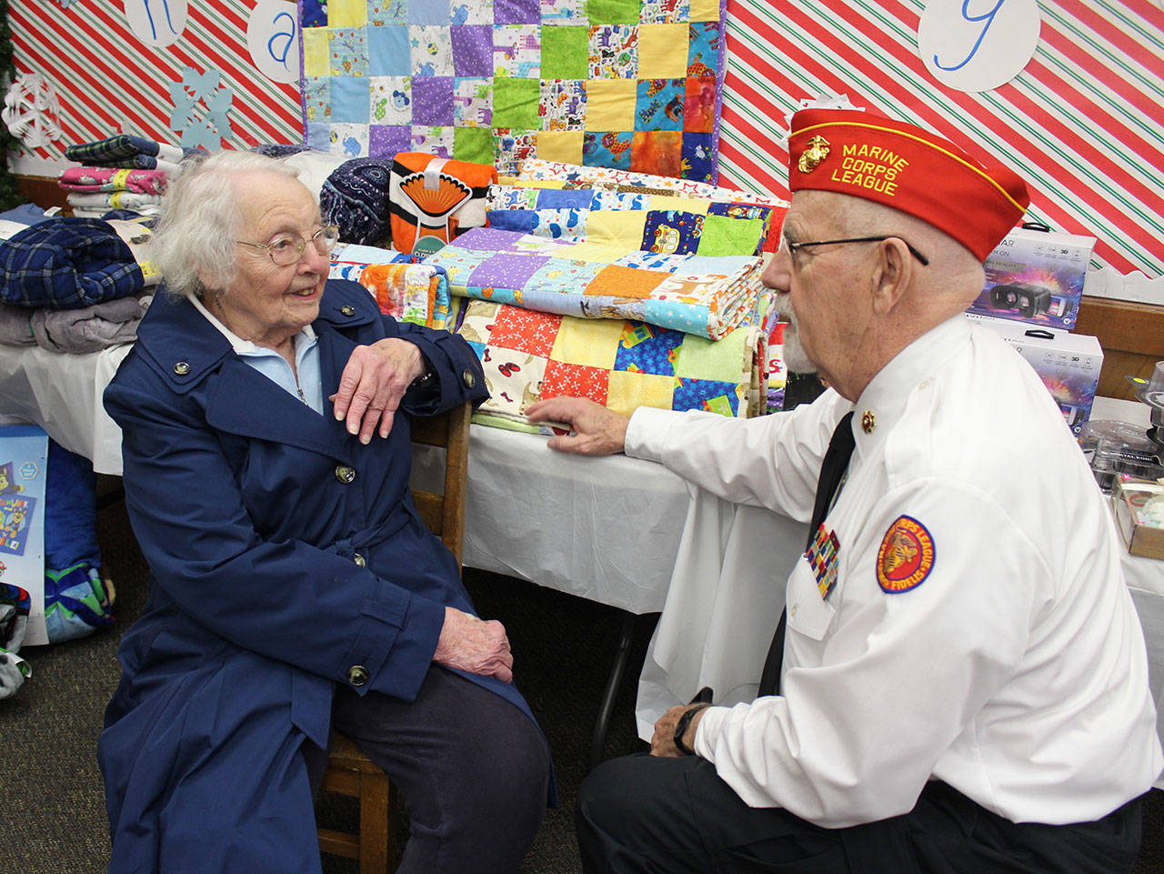 Frank Thorton, of Marine Corps League Detachment 1451, speaks with Ginny Mayer, who stitched together four dozen kid-size quilts. They are being given away to families in need through Toys for Tots and Holiday House at South Whidbey Community Center. (Photo by Patricia Guthrie/Whidbey News Group)