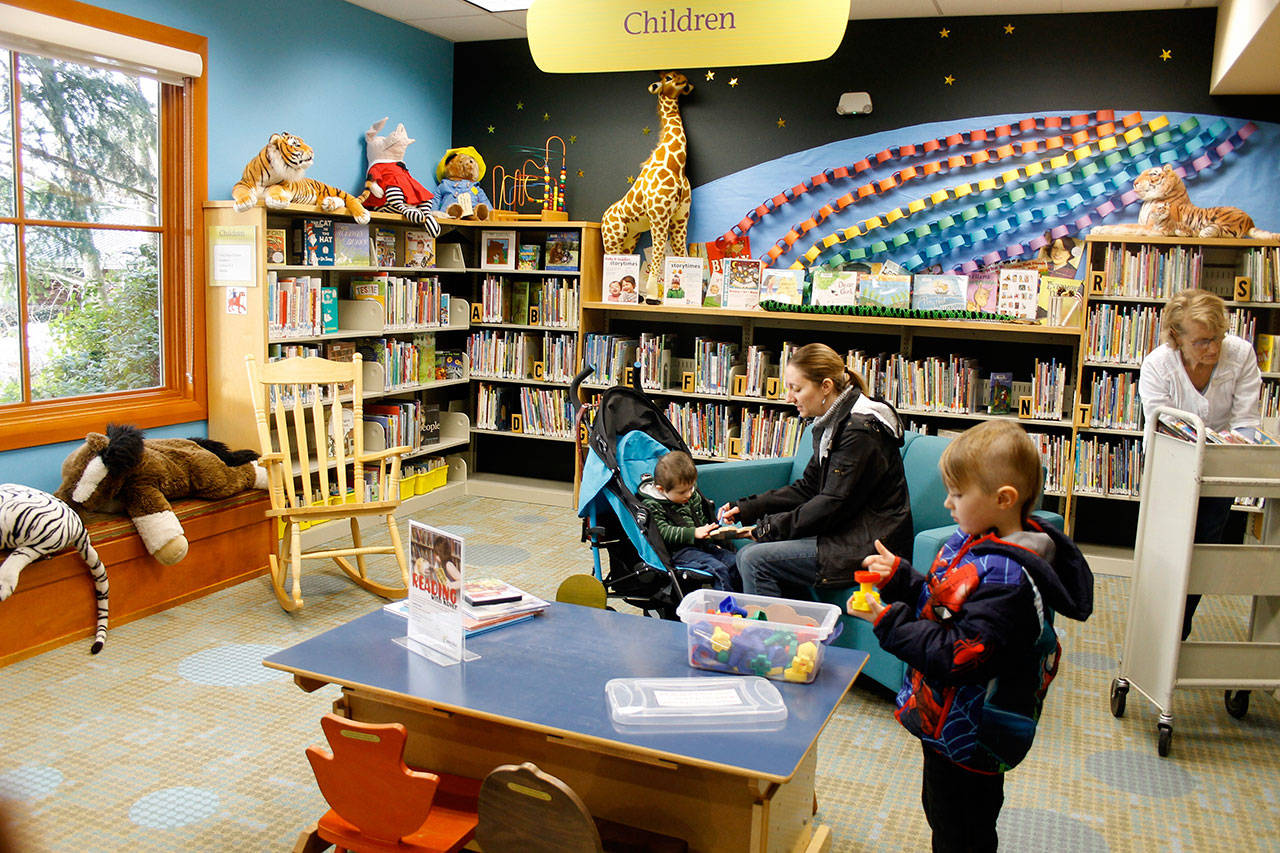 Vincent Van Houton, 5, looks over toys and books in the children’s section of Freeland Library as his mother, Andrea Van Houton, attends to little brother Gavin. The library received new carpeting, furniture and brighter walls during a sprucing up. On the right, Erica Even restocks books.(Photo by Patricia Guthrie/Whidbey News Group)