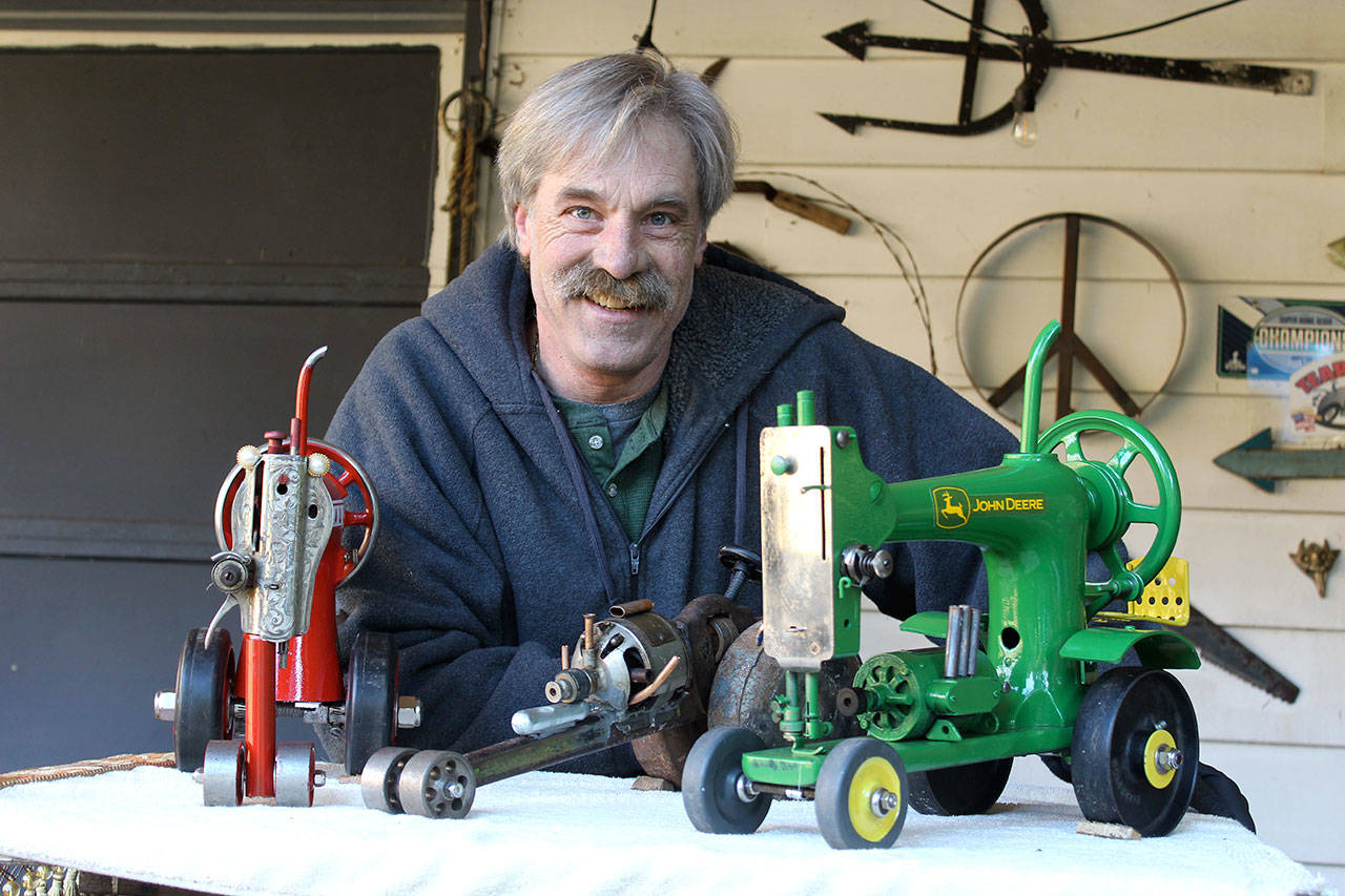 John Norris shows his miniature red Farmall and John Deere green tractors he created out of sewing machines. In the middle is a drag car model made from a pipe wrench. His creations appear at the current Bayview Cash Store recycled art show. (Photo by Patricia Guthrie/Whidbey News Group)