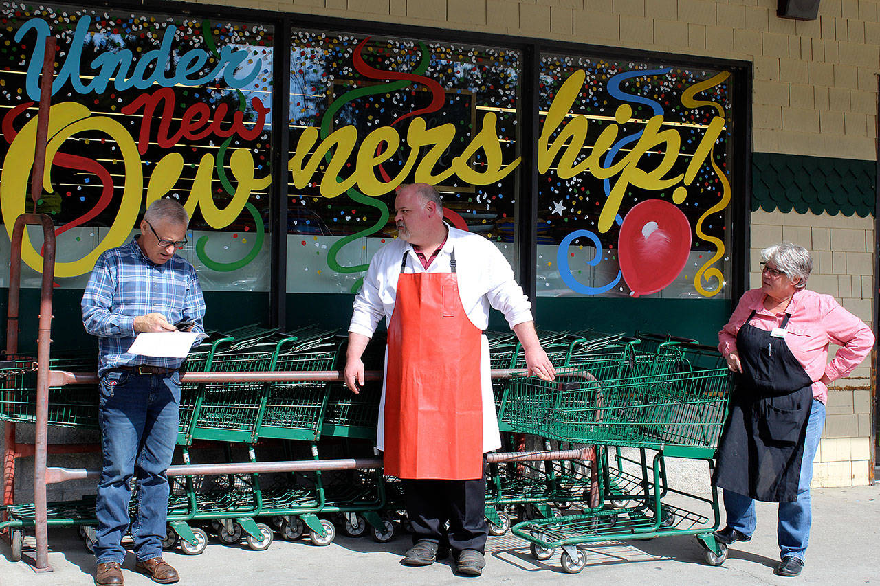 Wearing his red butcher’s apron, Tom Brierley, new owner at Ken’s Korner Red Apple Market in Clinton, talks with a vendor as manager Robin Thompson, right, looks on. Among Brierley’s plans are lowering prices and getting more involved with the community. (Photo by Patricia Guthrie/Whidbey News Group)