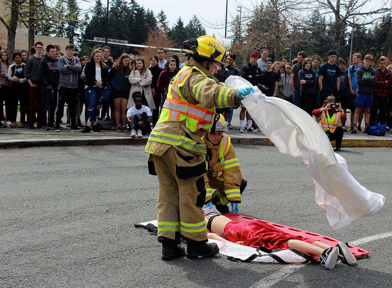 South Whidbey Fire/EMS responders place a white sheet over victim Emma Gilbert who died from head injuries after being thrown through the windshield of a car driven by her pretend and real  boyfriend, Aryeh Rohde. Leadership students organized the demonstration that also involved an assembly. (Photo by Patricia Guthrie/Whidbey News Group)