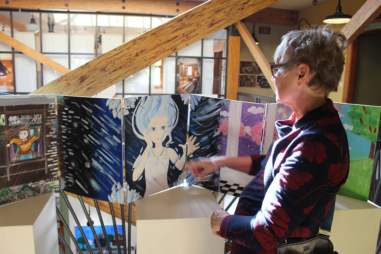 Peggy Gilmer looks over a ten-panel piece called “Unhinged Reflections” by student artist Casey Rogers at the “Art with a Message” exhibit. On view until June 9 at Bayview Cash Store, the annual all-island high school art show is sponsored by Goosefoot. (Photo by Patricia Guthrie/Whidbey News Group)