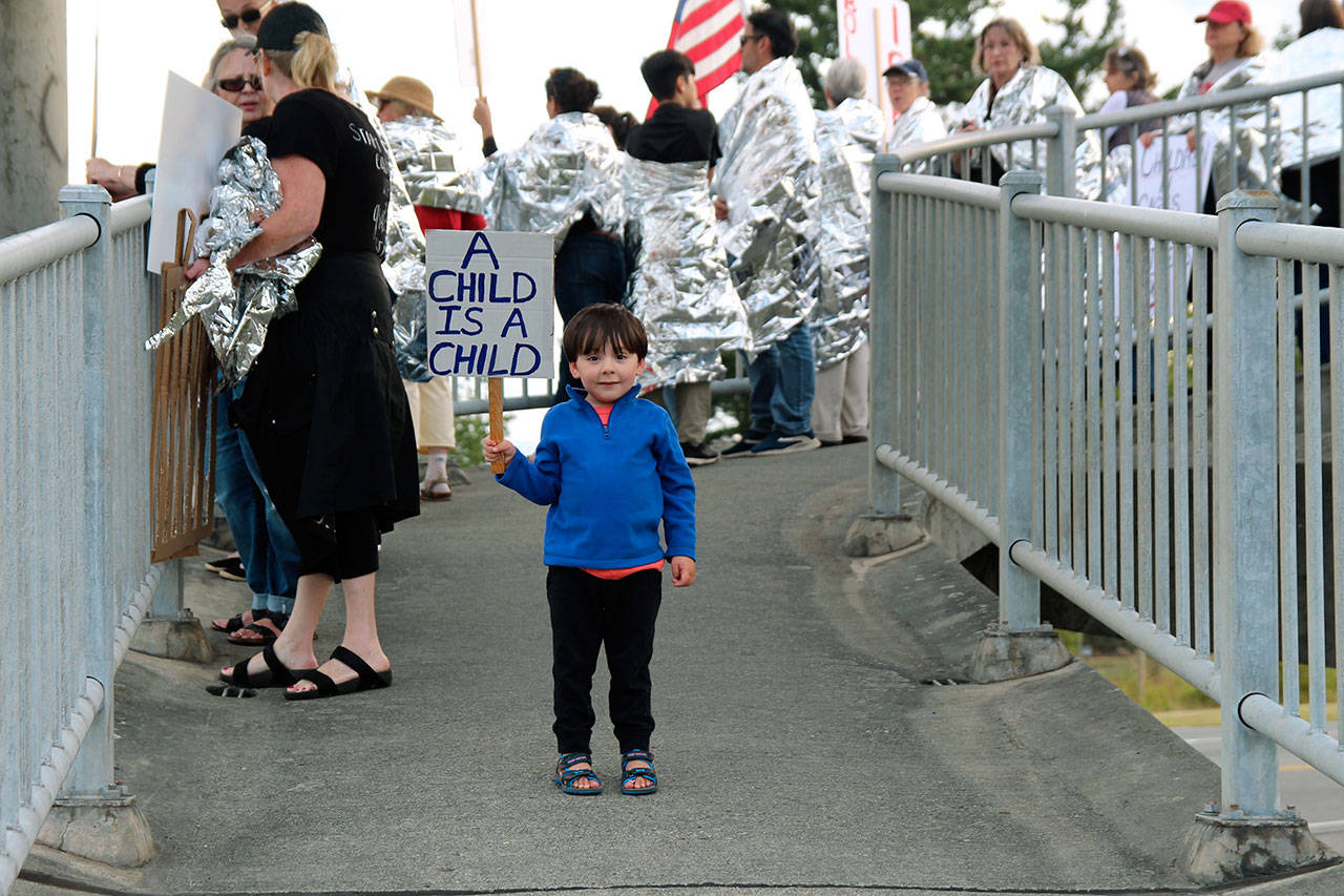 Demonstrators in Coupeville Friday evening hold up signs protesting immigration policies as part of a national “Lights for Liberty” event.Everson Welch, 3, attended with his family. (Photo by Maria Matson/Whidbey News-Times)