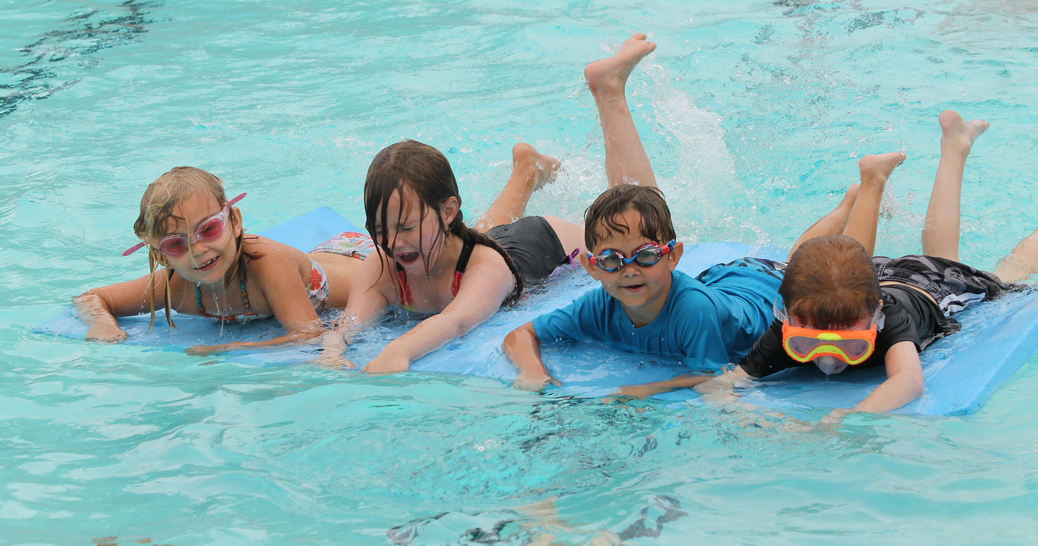 Eleanore Hunsaker, left, Klara Hanson Nikulina, Dreyke Mendiola and Curtis Hastings show a variety of emotions while floating on a foam mat during a swim lesson Thursday. (Photo by Jim Waller/South Whidbey Record)
