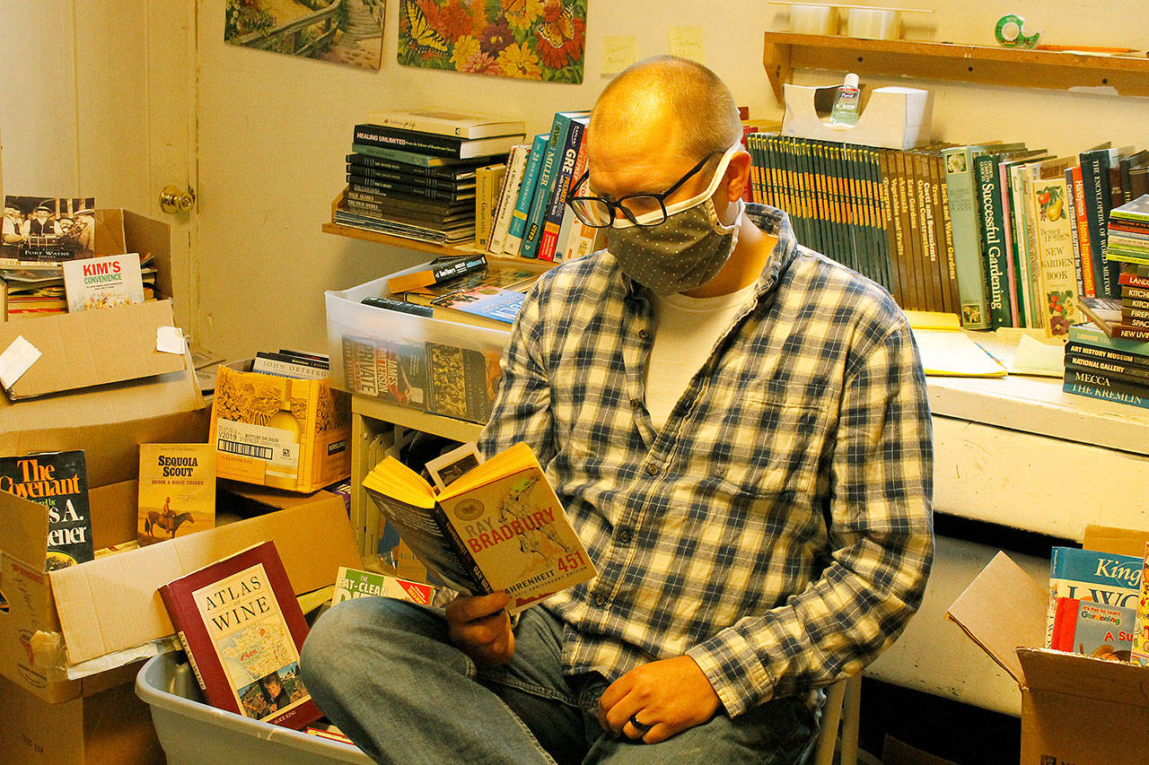 Photo by Kira Erickson/Whidbey News-Times                                Surrounded by the 500 books he has collected during the last two weeks, Kevin Tyler Lucas reads one of his favorite novels, “Fahrenheit 451.”