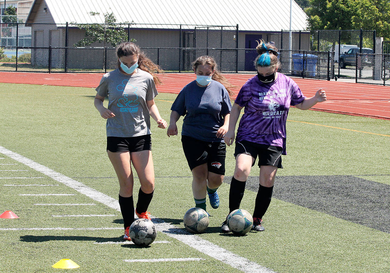 Maggie Root, left, Heidi Hogarth and Brittany Day, wearing masks as required, work on dribbling during an offseason workout in Oak Harbor Monday. (Photo by Jim Waller/Whidbey News-Times)
