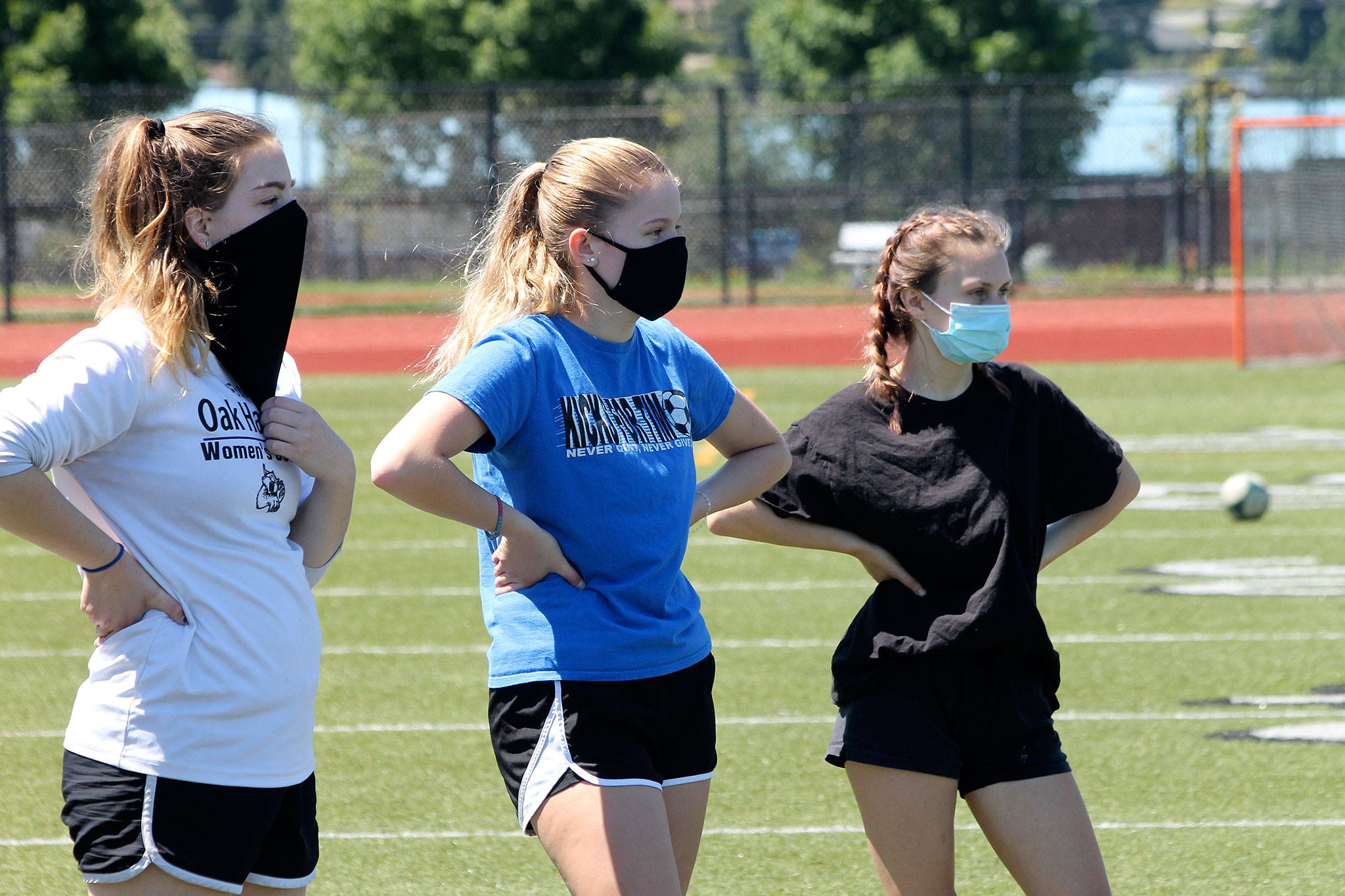 Oak Harbor’s Emma Erskine, left, Bailey Trease and Emily Miller listen to instructions before a drill at offseason workouts Monday. Health guidelines require athletes to wear masks when within six feet of each other. (Photo by Jim Waller/Whidbey News-Times)