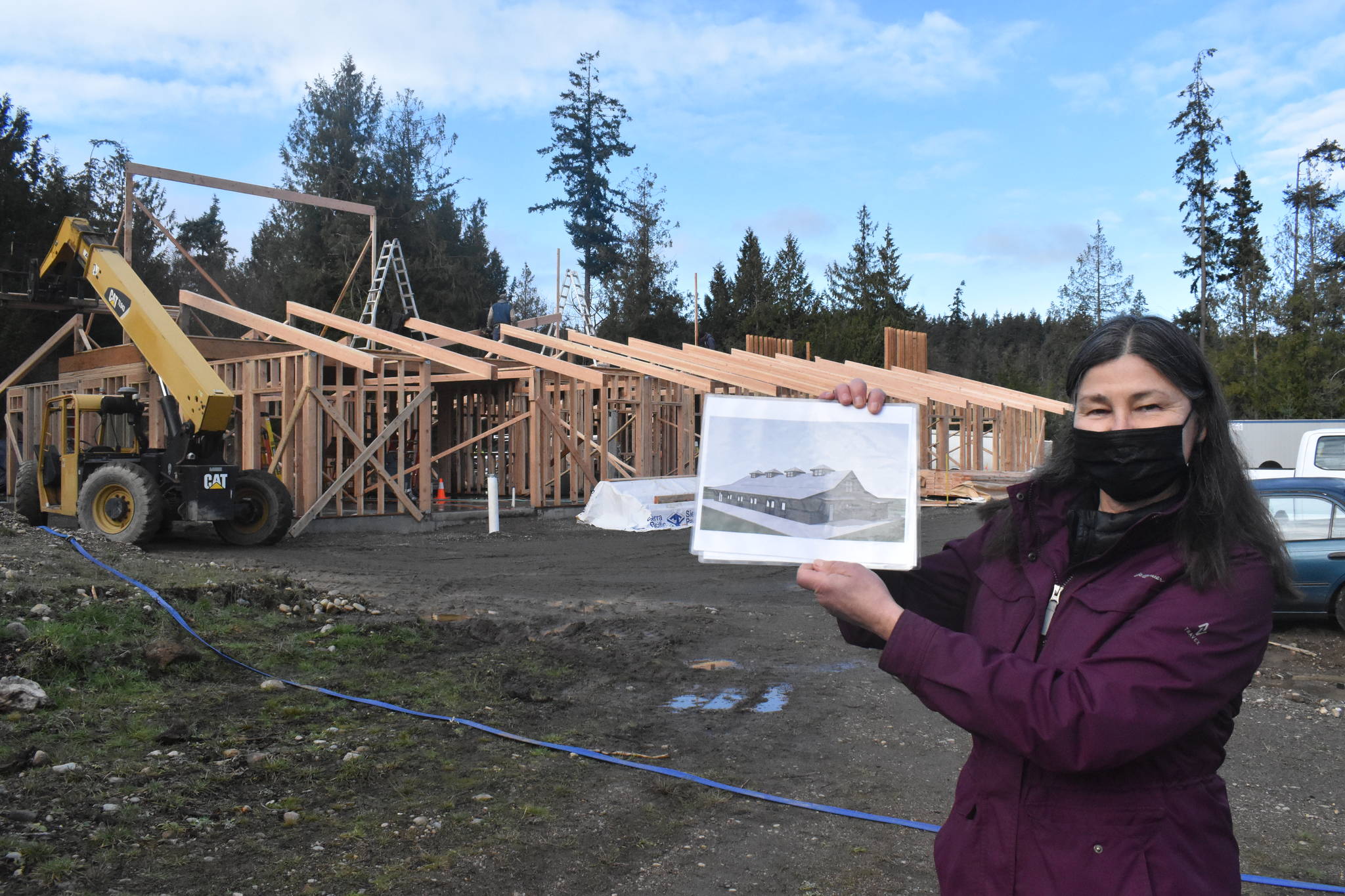 Sue Meinzinger holds up a drawing of what the Canine Condo in the background will eventually look like. There are two other buildings planned for the site. Photo by Emily Gilbert/Whidbey News-Times