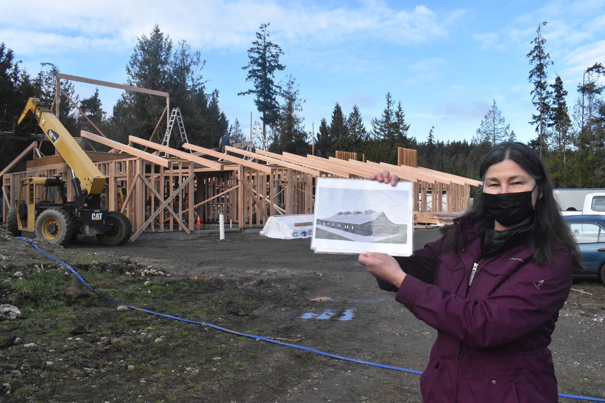 Sue Meinzinger holds up a drawing of what the “Canine Condo” in the background will eventually look like. There are two other buildings planned for the site. Photo by Emily Gilbert/Whidbey News-Times