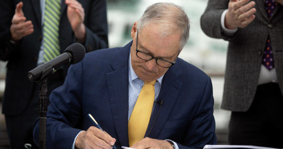 Governor Jay Inslee signs SB 5974 into law during a bill signing Friday, March 25, 2022, outside the ferry terminal in Mukilteo, Washington. (Ryan Berry / The Herald)
