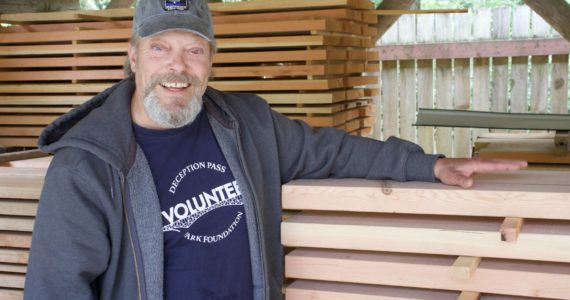 Wallgren with wooden planks he makes picnic tables out of. (Photo by Rachel Rosen/Whidbey News-Times)