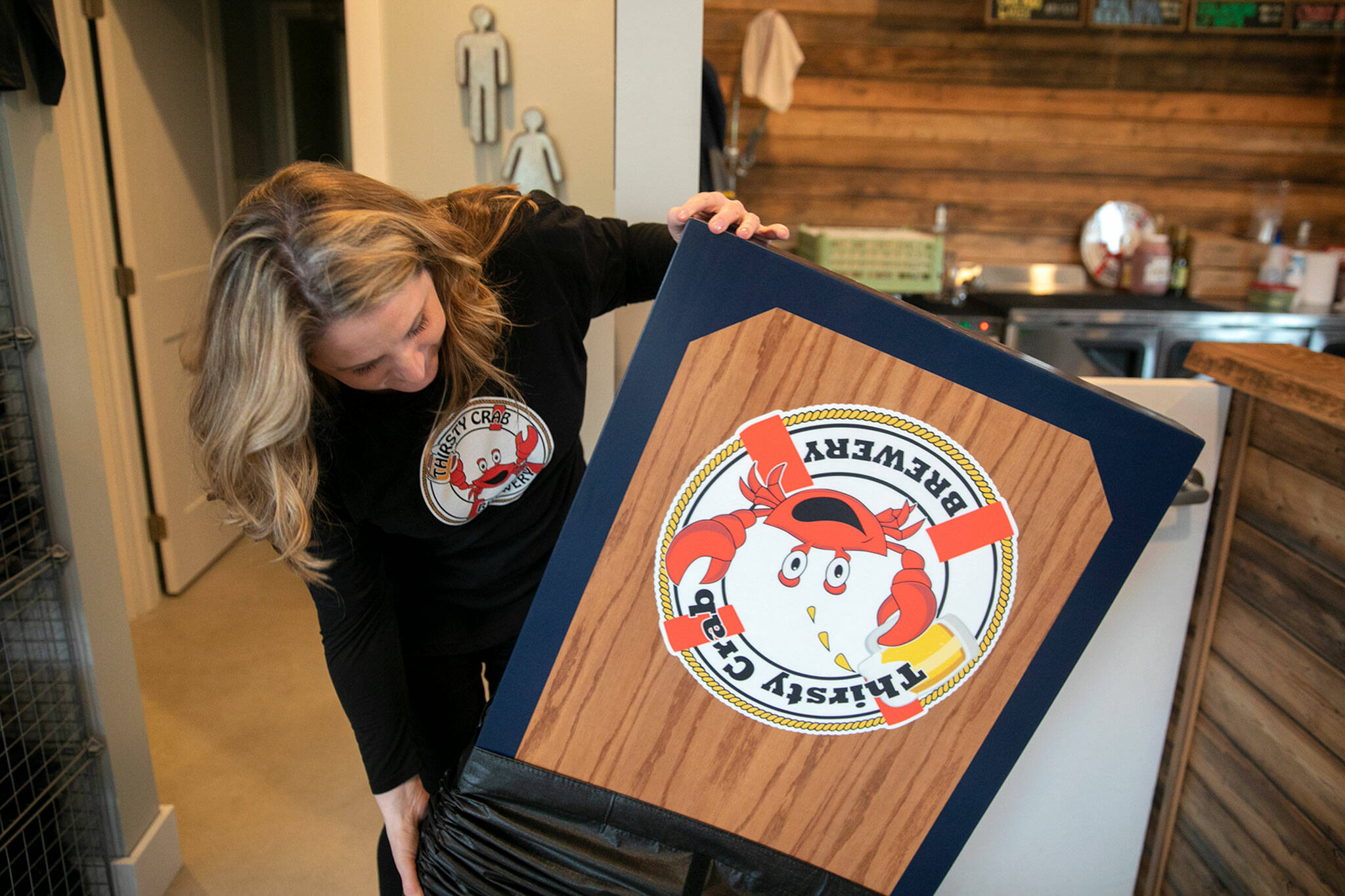 Erin Hanson shows off one of the custom bean bag toss boards available to customers at Thirsty Crab Brewery in Clinton. (Ryan Berry / The Herald)