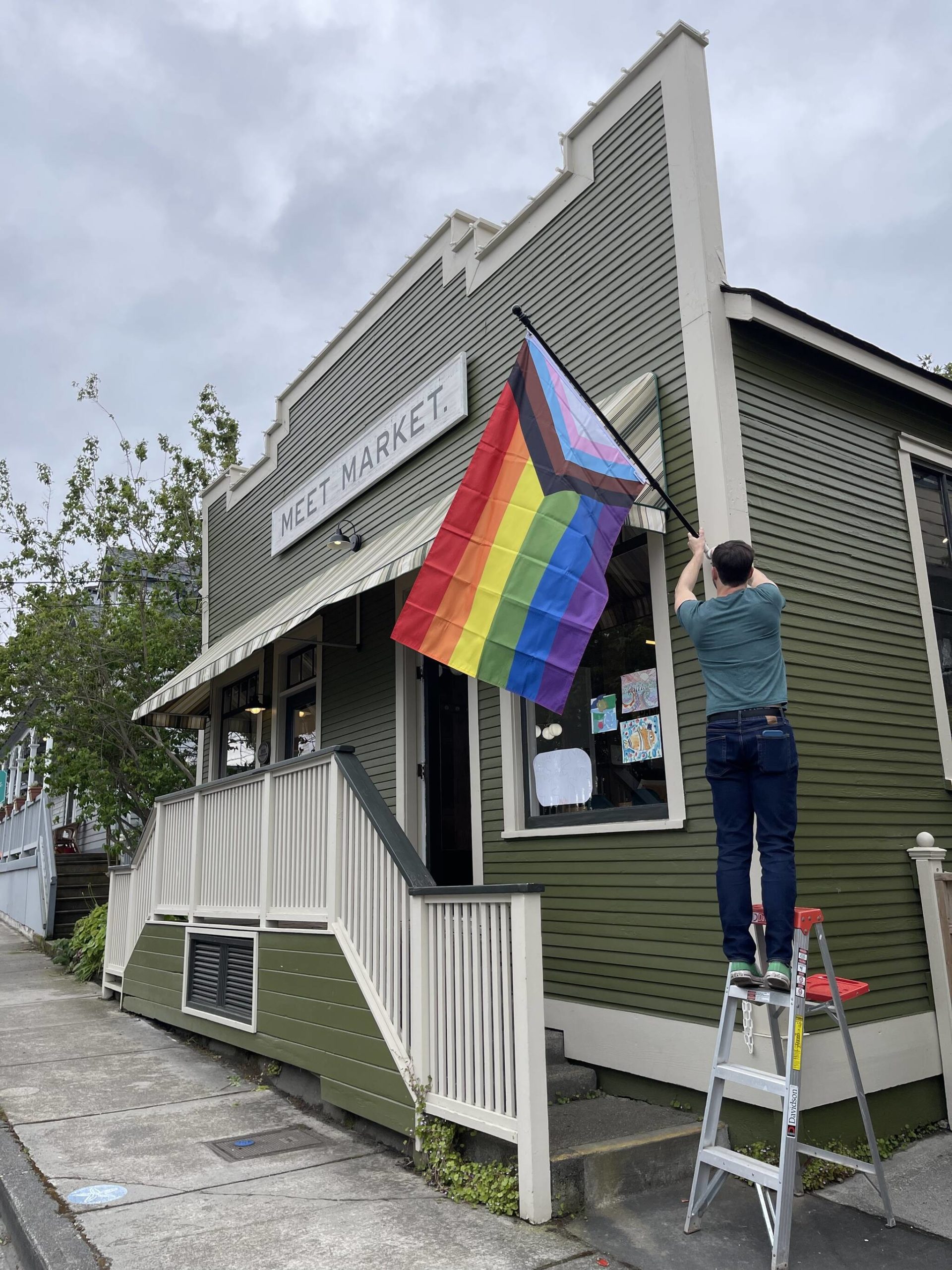Business owner Cade Roach hangs a pride flag outside of Meet Market. (Photo provided)