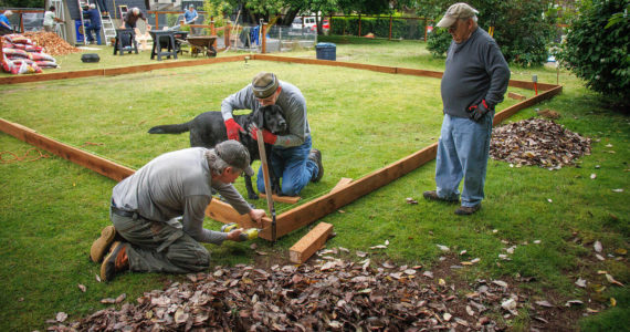 From left to right, Jan-Marc Jouas, Russ DeWolfe and David LaBreque of Rotary Club of South Whidbey Island, with assistance from service dog Theo, work on building an enclosure for a playground in the backyard of the House of Hope.(Photo by David Welton)