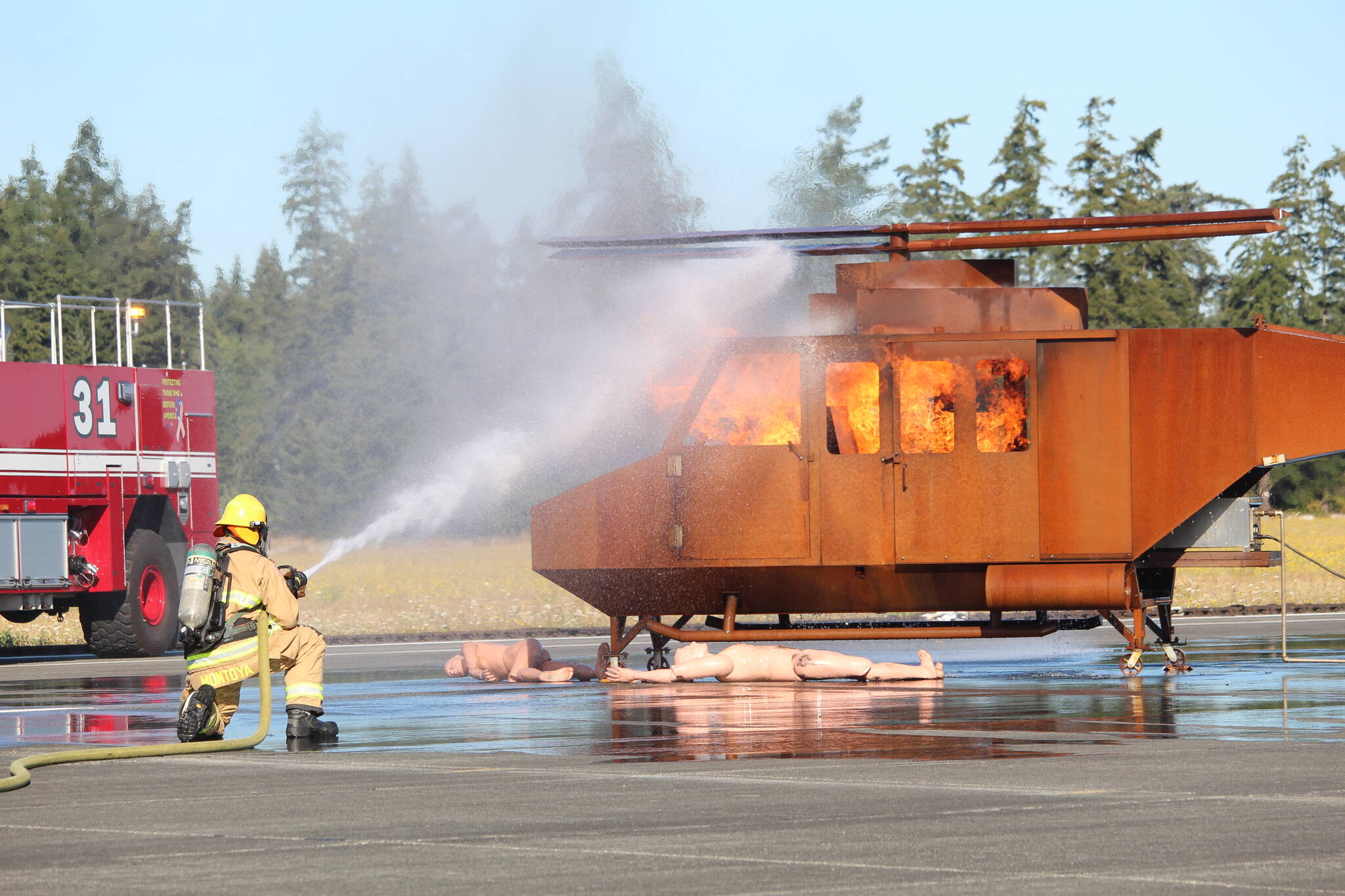 Photo by Karina Andrew/Whidbey News-Times
A Navy firefighter aims a hose at a helicopter fire during an emergency simulation at Outlying Field Coupeville Aug. 17.