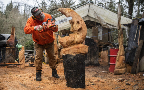 Steve Backus works on the details of a moon carving at his outdoor workshop in Clinton. A Dec. 2 fire destroyed his studio in the former sawmill on the 4-acre Glendale Road property that houses his Big Shot Woodcarving business and home. (Olivia Vanni / The Herald)
