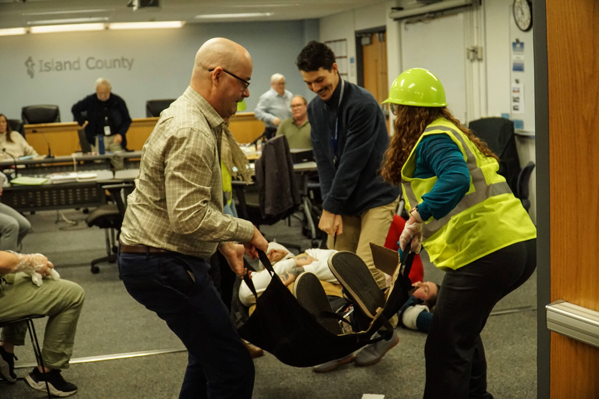 Island County Planning Manager Michael Jones, Board Clerk Jennifer Roll and others carry an actor during an earthquake demonstration at the commissioners’ meeting on Wednesday. (Photo by Sam Fletcher)