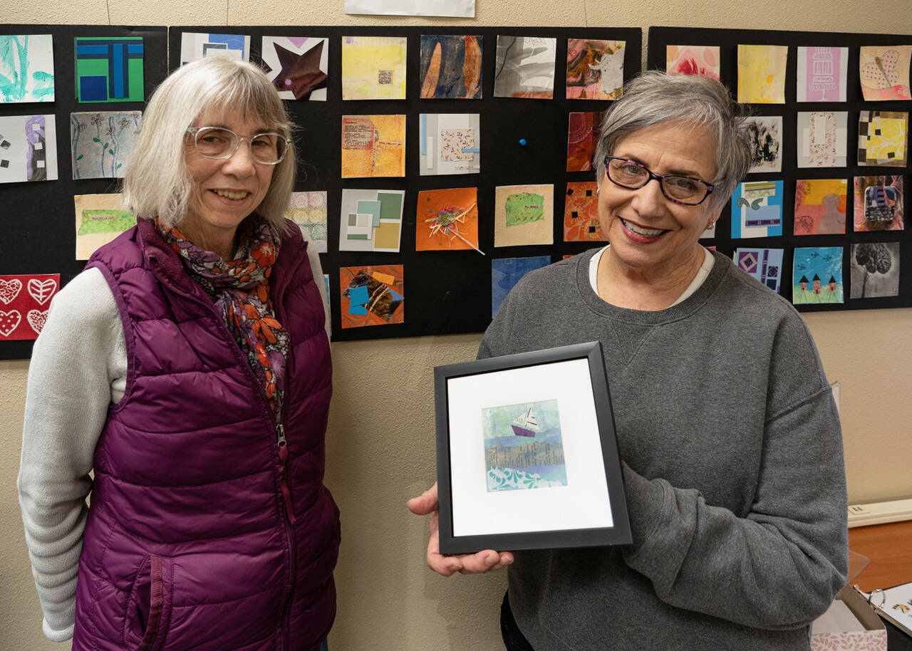 Artist Cyndy Jensen, right, holds up a framed art piece made by Karen Rothboeck, left. (Photo by David Welton)