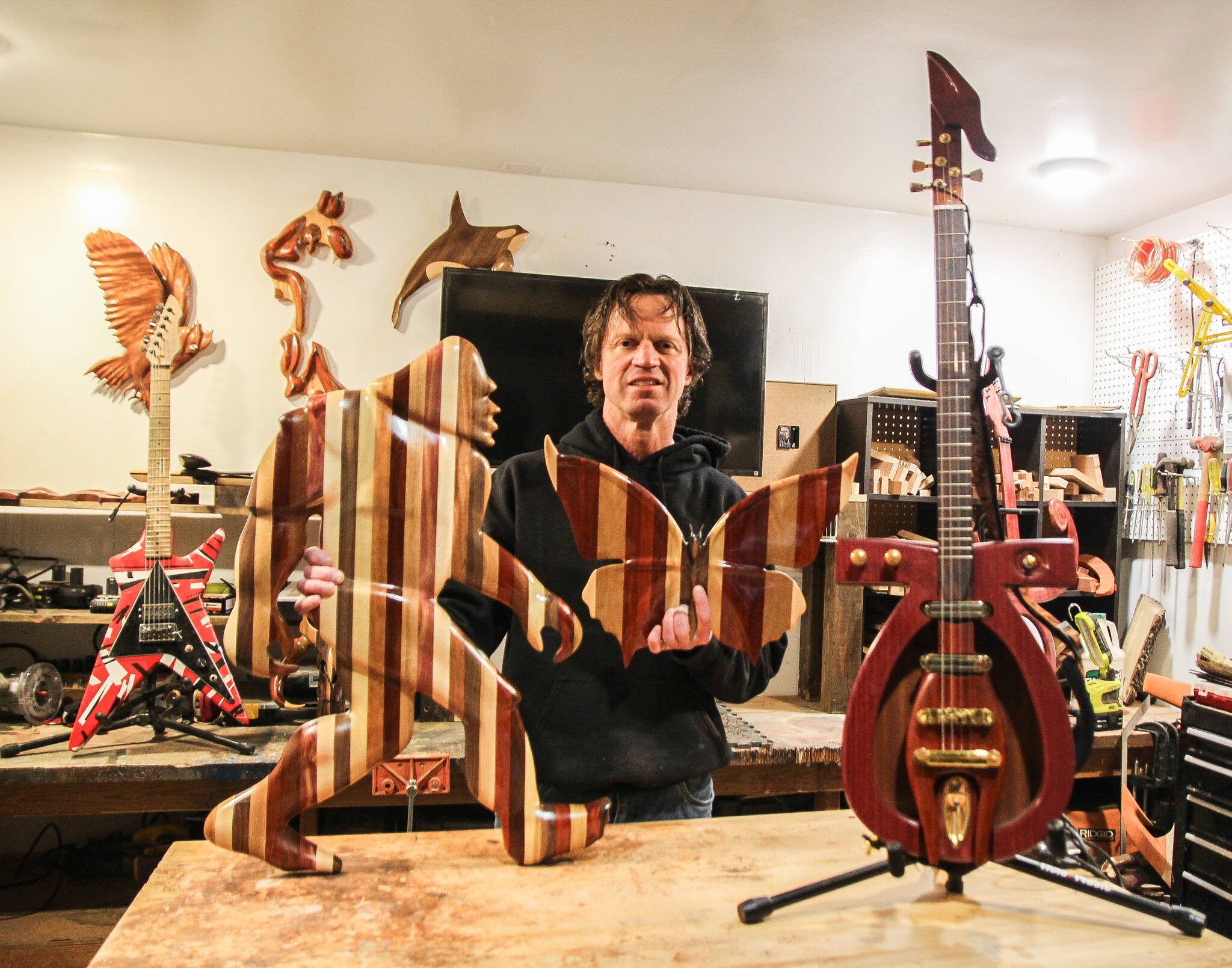 Chad Pilkington, a wood carver who lives in Oak Harbor, poses in his garage with some of his creations: Bigfoot, a butterfly and a hieroglyph guitar. (Photo by Luisa Loi)