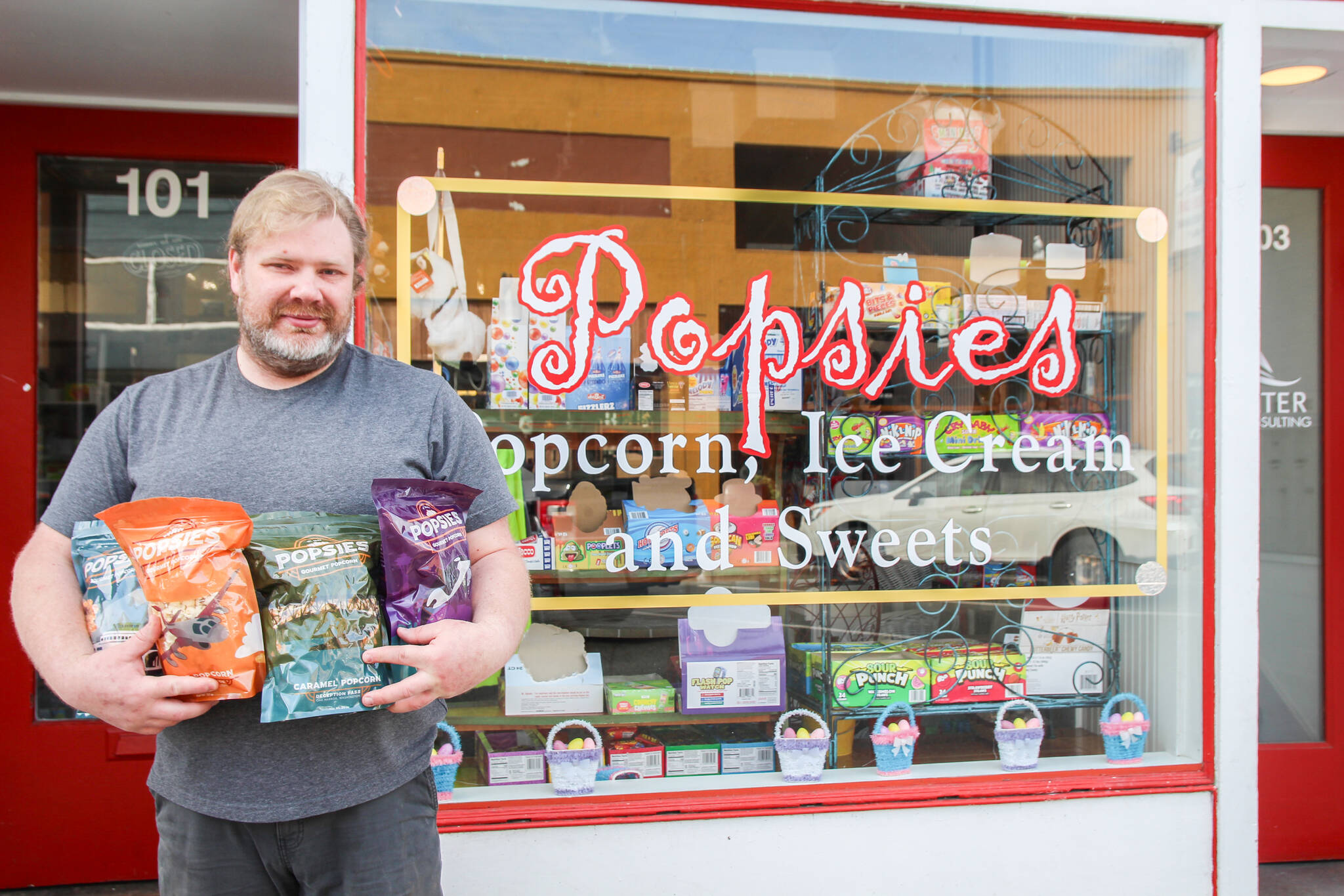 Andy Plumlee stands in front of Popsies, a sweet treats store in downtown Oak Harbor, while holding bags of flavored popcorn.