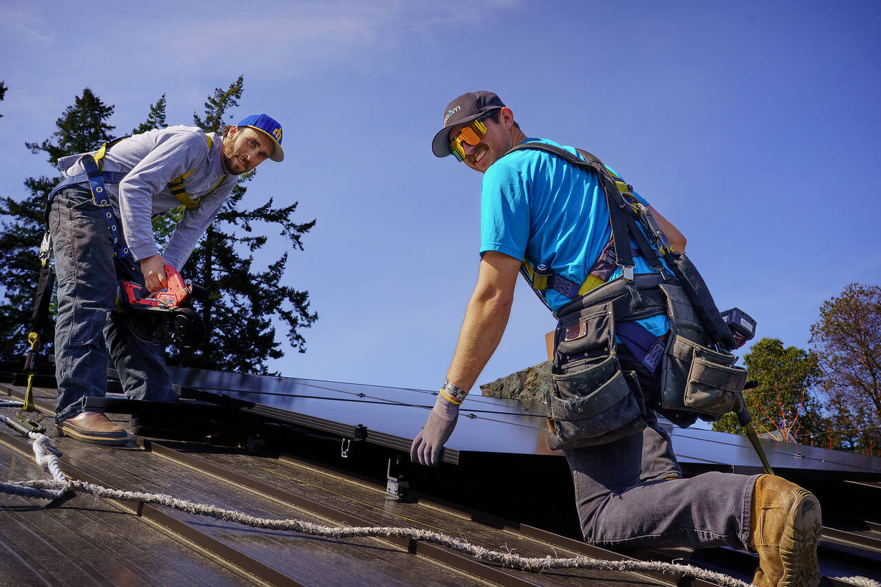 Will Glasgow and Nick Minden from Blossom Solar install an array of panels onto the Clinton Community Hall roof this week. (Photo by David Welton)