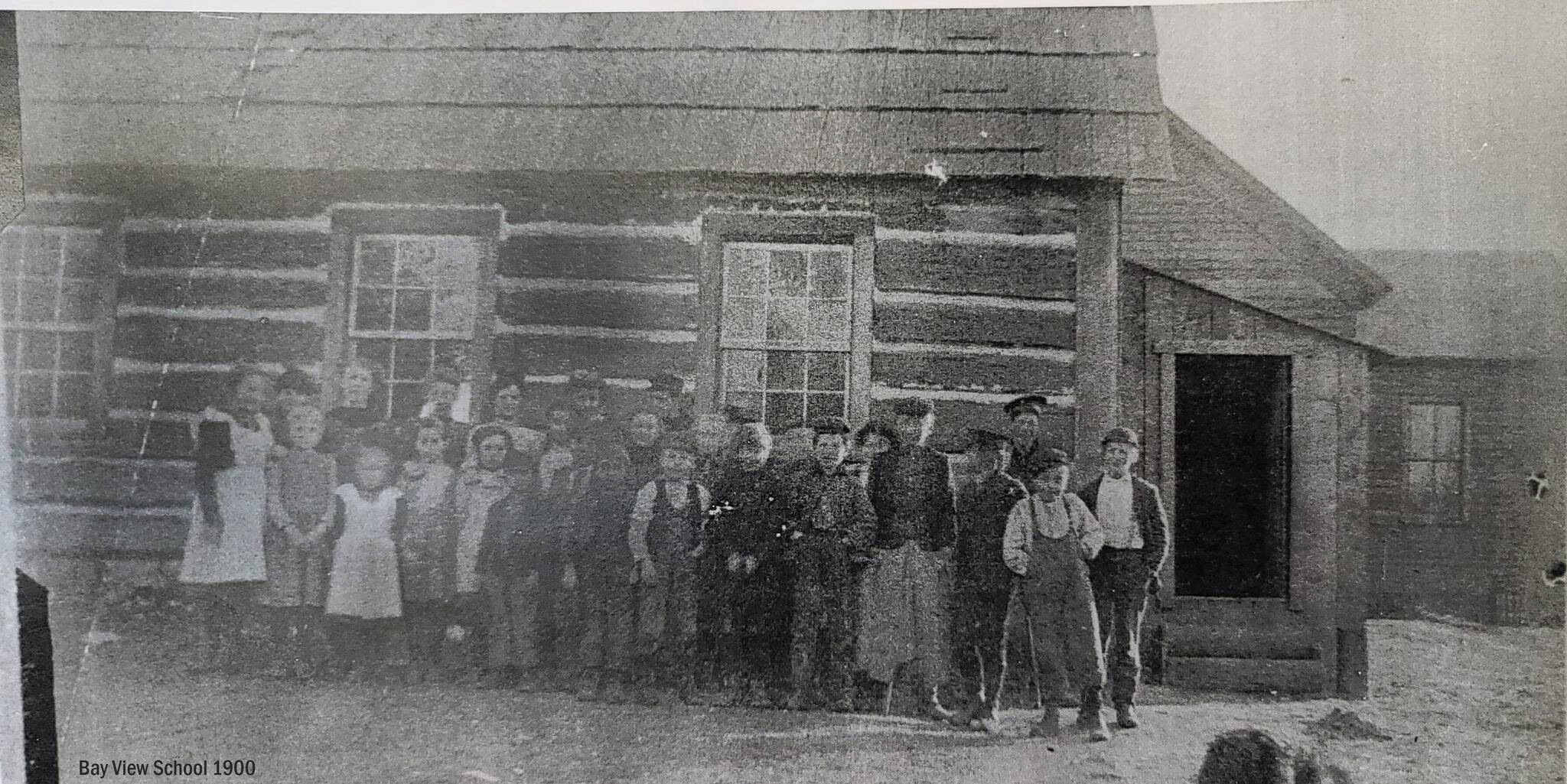 Students stand in front of the log cabin building that was later replaced by the white schoolhouse known today as the Bayview School (Photo courtesy of the Island County Historical Society)