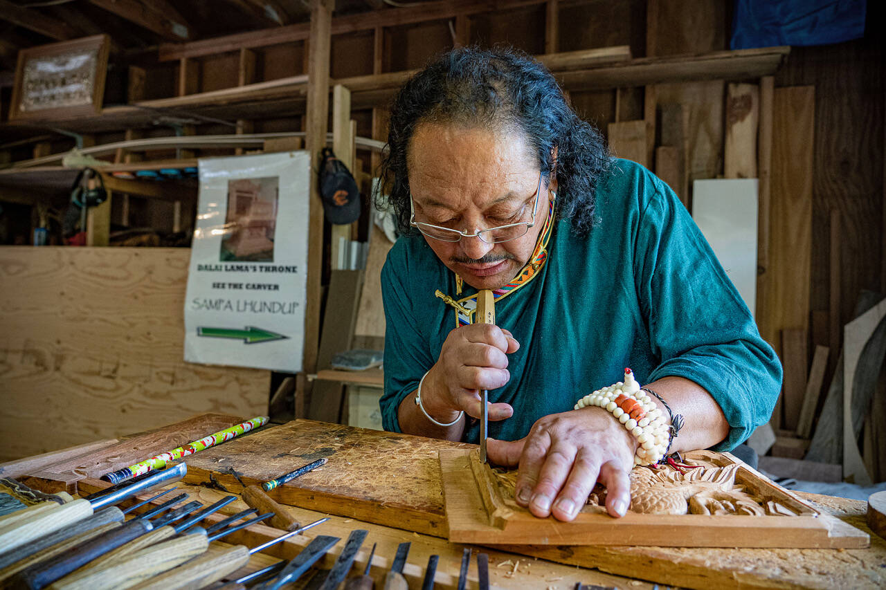 (Photo by David Welton) Sampa Lhundup works on a carving of a Tibetan bird in his studio. A sign in the background proudly proclaims him as the carver of the Dalai Lamas teaching throne.