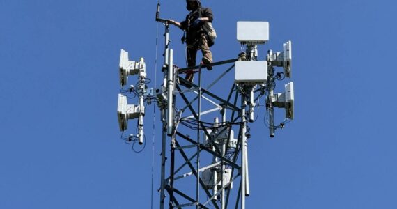 Astound technician installing fixed wireless network transmission devices atop existing headend tower.
