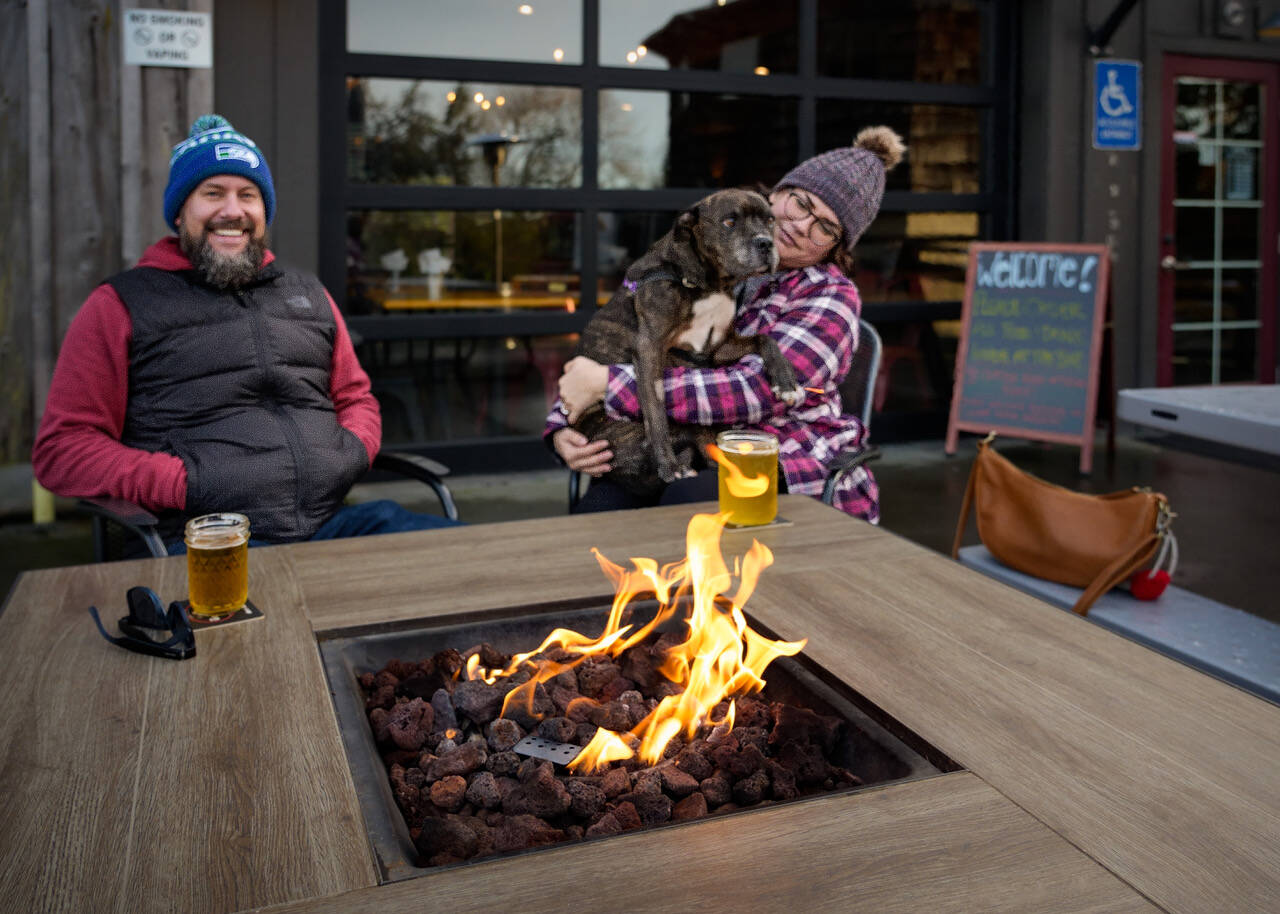 Photo by David Welton. Freeland residents Derek and Kaitlin Robinson cozy up around the firepit with their 12-year-old pitbull mix, Aggie, at The Barnyard.