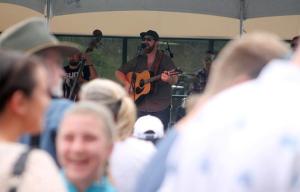 Top: Tanner McInerney of Weatherside Whiskey Band sings during one of the first performances Saturday at Choochokam Arts Festival in Langley. Right: Barry Crust of University Place burns a design into a driftwood walking stick in his Beyond the Beach tent on First Street. Above: Joel Sexton slices up ribs and brisket for an eager line of Choochokam visitors Saturday.