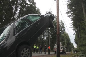 Emergency responders evaluate a Toyota Camry that slid off the road and up the guy-wires of a power pole.