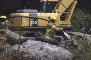 Herschel Rostov soaks the charred ground and burned logs at Ray Gabelein Jr.’s property on Bayview Road the morning of July 11.