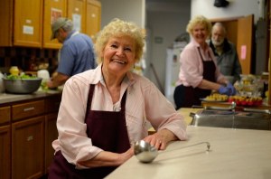 Jean Matheny poses for a picture at Soups On. Behind her are volunteers Rick Klein