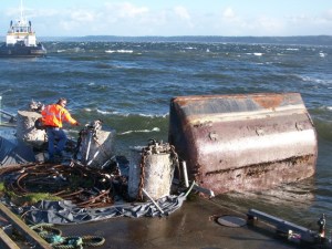 A Neptune Marine employee scurries to secure a sunken work barge in Monday morning’s storm. Two small barges sank in the strong wind and work to refloat them started in heavy rain Tuesday morning. In the background is the new tug built by Nichols Brothers.