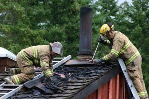 Fire District 3 Capt. Forrest Hughes and firefighter Brandon Callahan remove pieces of a burning roof at the scene of a house fire in Langley Monday morning.