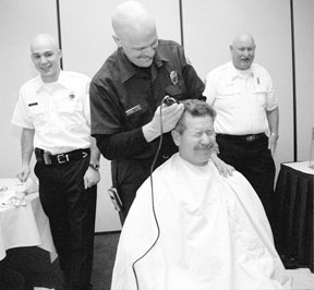 Robin Flem makes the first furrow into fire Chief Don Smith’s hair at a South Whidbey Kiwanis Club meeting Thursday as other clippered firefighters Eldon Baker