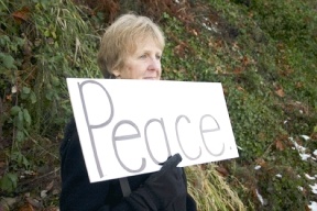 Linda Morris stood silently holding a "Peace" sign in a line of women Friday. The Women in Black lined the road from the ferry dock in Clinton to protest violence in the world.