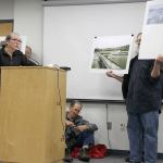 Patricia Guthrie / Whidbey News Group                                Steve Erickson holds up signs showing the disputed Wonn Road beach as Jane Seymour, attorney for the group Island Beach Access, urges Island County commissioners to reject a settlement that ultimately was approved in a 2-1 vote.