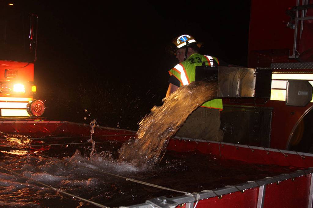 Firefighters fill a basin with water so it can be pumped to the engine near the burning Smith Barn. Photo by Ron Newberry/Whidbey News-Times