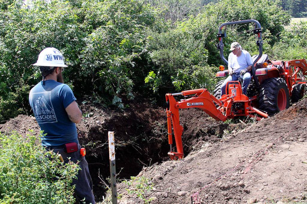 Craig Holmquist uses an excavator Monday, May 22, 2017 to dig a hole for a new vault toilet that will be installed in June near the office of Ebey&rsquo;s Landing National Historical Reserve in Coupeville. Carl Sholin, an archaeologist with the National Park Service, monitors the dig. The Reserve will be busy with several projects this summer as it braces for an increasing number of visitors. Photo by Ron Newberry/Whidbey News-Times